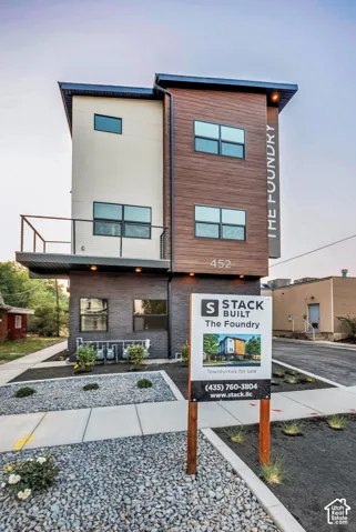 Modern multi-story exterior featuring composite wood-finish siding, dark masonry lower level, attached metal-railing balcony, and inset recessed lighting