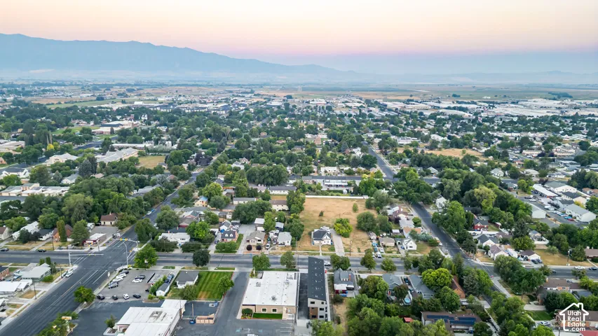 Aerial perspective featuring a landscape of mature trees, mountain range backdrop, and paved street access