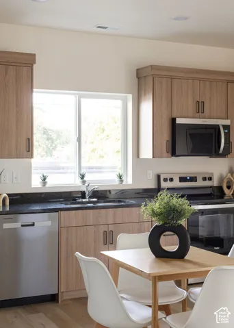 Kitchen featuring wood-finish cabinetry, dark stone-style countertops, stainless steel appliances, and a window above the sink