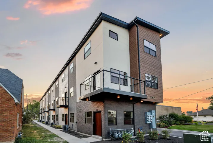 Modern multi-story exterior featuring a mix of masonry, horizontal siding, and wood-finish paneling, complemented by metal-railing balconies and expansive windows
