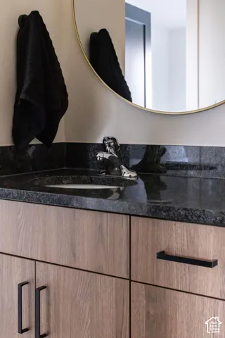 Floating vanity featuring wood-finish cabinetry, dark stone countertop, integrated sink, circular mirror with metallic frame, and matte black hardware