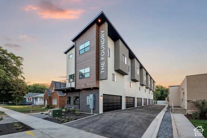 Contemporary multi-level exterior featuring wood-finish siding, dark brick lower facade, multiple cantilevered bays, metal roofing, and multiple garage bays