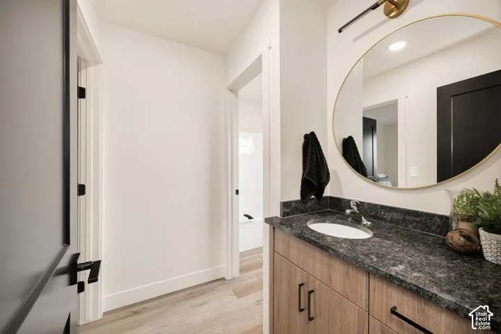 Vanity featuring wood-finish cabinetry, a stone-composite countertop with an integrated basin, a gold-rimmed oval mirror, and matte black hardware