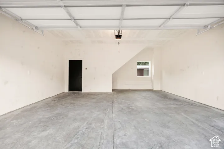 Finished garage featuring a high ceiling, concrete flooring, a single-panel door, and a window for natural light