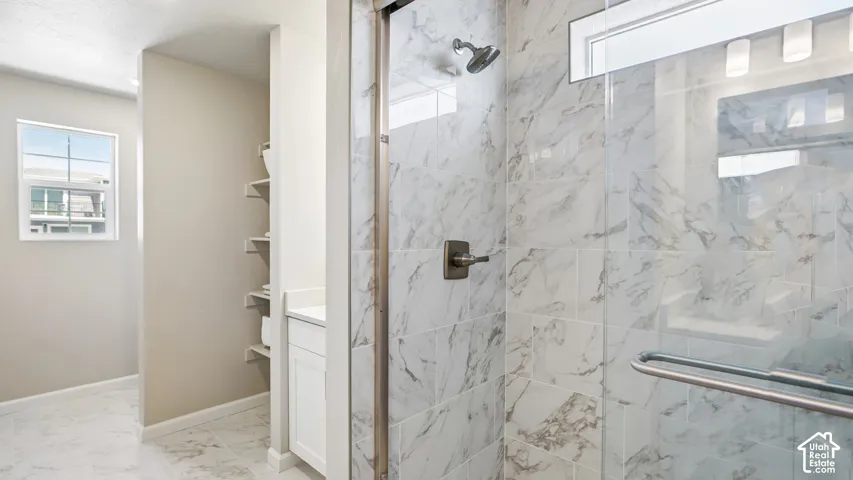 Walk-in shower with floor-to-ceiling stone-finish tile surround, glass enclosure, and metallic hardware, featuring stone-finish tile flooring, built-in shelving, and a horizontal transom window