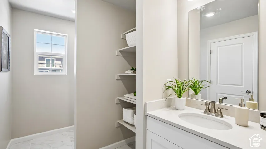 Bathroom featuring a white vanity with a composite countertop, an oval under-mount sink, a wall-mounted mirror, built-in shelving, and a single-hung window