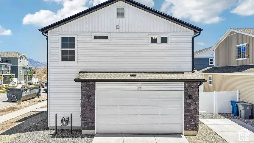 Two-story home exterior featuring horizontal white siding, stone veneer accents, an attached two-car garage, and asphalt shingle roofing