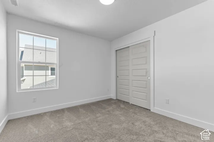 Neutral-toned carpeted flooring, sliding closet doors with paneled detailing, single-hung window with a grid pattern, and crisp white wall trim