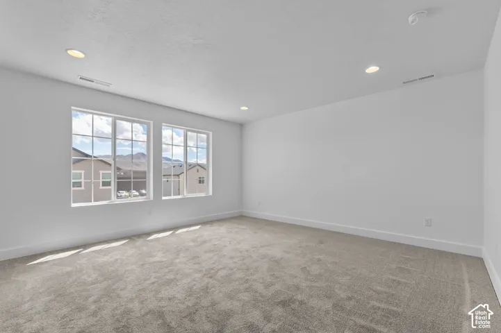 Neutral-toned carpeted flooring, recessed lighting, and large windows providing natural light