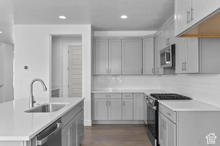 Kitchen featuring grey shaker-style cabinetry, white quartz countertops, white subway tile backsplash, stainless steel appliances, and wood-finish flooring