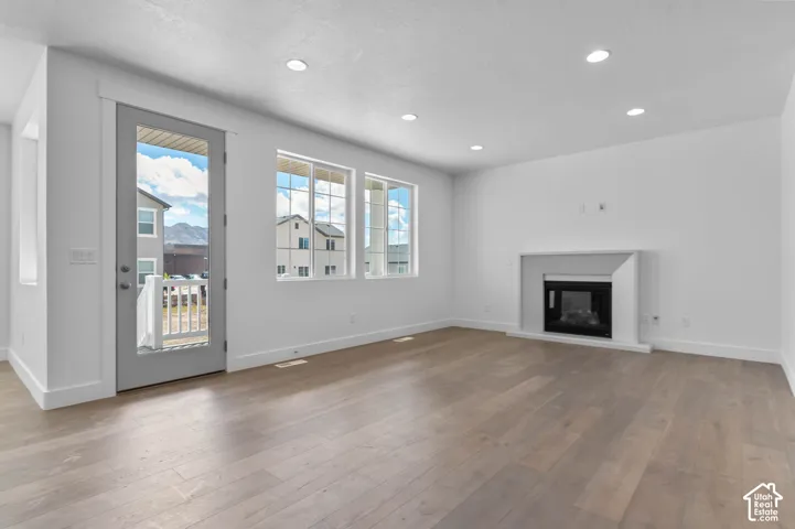Living area featuring wood-finish flooring, recessed lighting, double-pane windows, a fireplace with a minimalist surround, and a glass-paneled exterior door