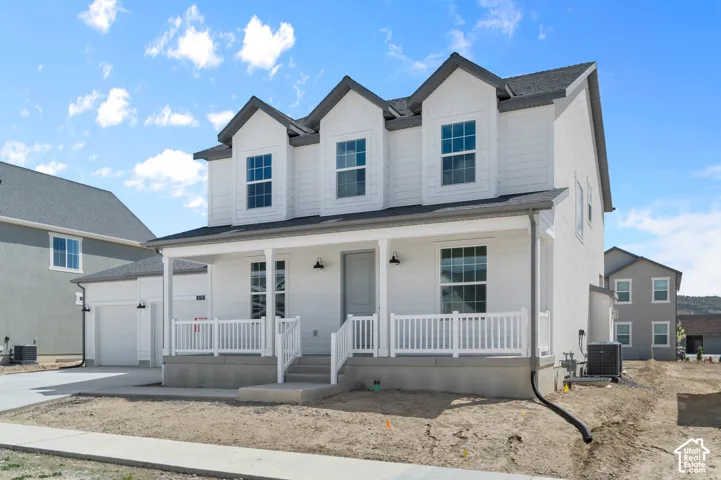 Two-story exterior featuring horizontal siding, a covered front porch with white railing, three prominent dormer windows, and an attached two-car garage