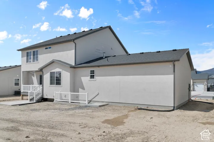 Stucco exterior featuring an asphalt shingle roof, multi-level design, white vinyl railing, and concrete patio space