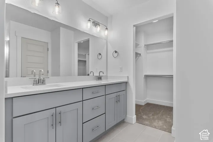 Dual-sink vanity with light-gray cabinetry, solid-surface countertops, full-width mirror, and three-light vanity fixture
