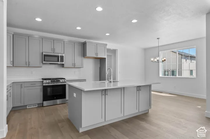 Kitchen featuring shaker-style grey cabinetry, white countertops, a central island with a built-in sink, recessed lighting, and wood-finish flooring