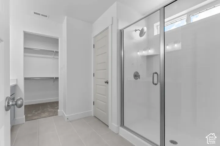 Glass-enclosed shower with brushed nickel fixtures, tile flooring, and walk-in storage area