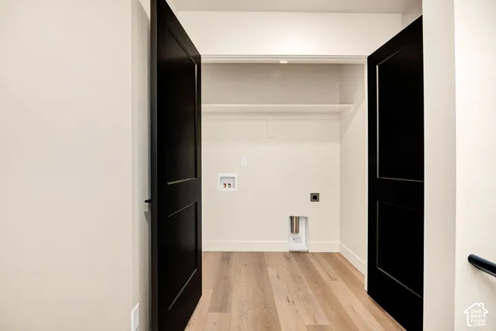 Utility closet featuring double shaker-style doors with matte black hardware, wood-finish flooring, and built-in shelving