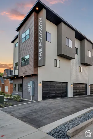 Modern multi-story exterior featuring composite siding, smooth stucco finish, stone veneer accents, integrated balcony with railing, and multiple private garage bays
