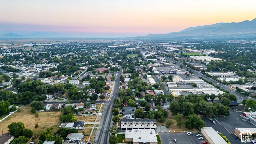 Aerial perspective featuring mature trees, a multi-unit structure, paved roadway, and a mountain range backdrop