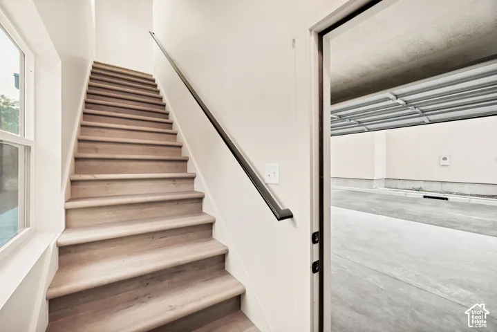Staircase featuring wood-finish treads and a matte black handrail, with an entryway providing direct access to the concrete-surfaced garage