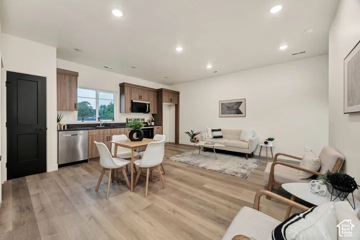 Open-concept living space featuring wood-finish flooring, recessed lighting, medium-tone wood cabinetry, a dark-toned stone-finish countertop, and a solid black interior door