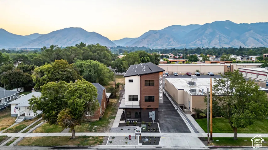 Three-story modern industrial exterior featuring dark masonry, horizontal wood-finish siding, and metal roofline, set against a backdrop of mountain scenery