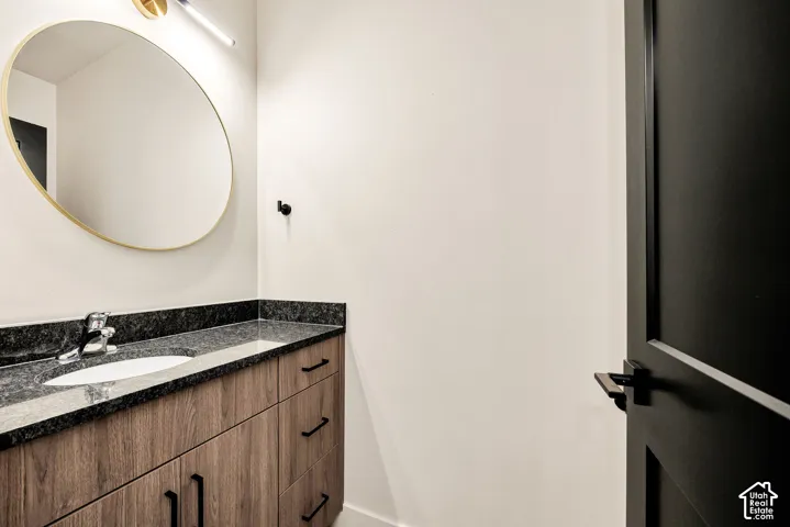 Vanity with wood-finish cabinetry, dark stone-style countertop, oval mirror with metallic trim, matte black hardware, and coordinated fixture
