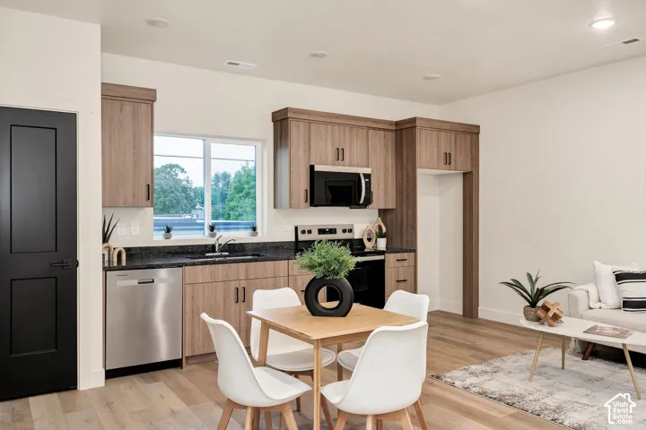 Kitchen featuring light wood-finish cabinetry, dark stone countertops, stainless steel appliances, recessed lighting, and wood-finish flooring