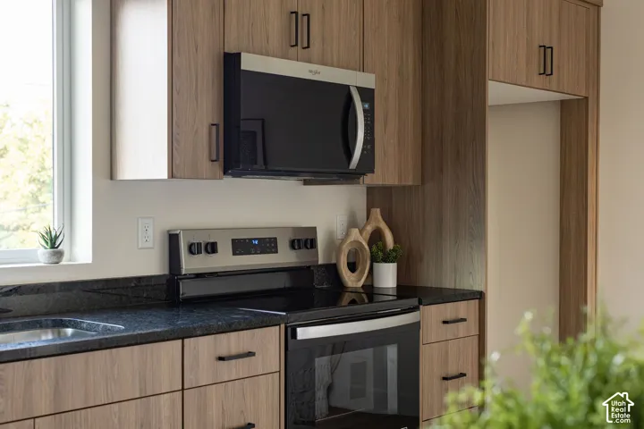 Kitchen featuring wood-finish cabinetry, dark stone-finish countertops, stainless steel electric range, and integrated stainless steel microwave
