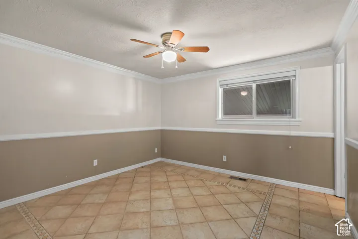 Room featuring tile flooring with decorative inlay, two-tone wall paint, chair rail molding, crown molding, and a central ceiling fan with integrated light fixture