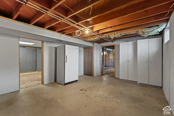 Unfinished utility area featuring exposed wood joist ceilings, concrete flooring, built-in white storage cabinetry, and solid-surface wall partitions