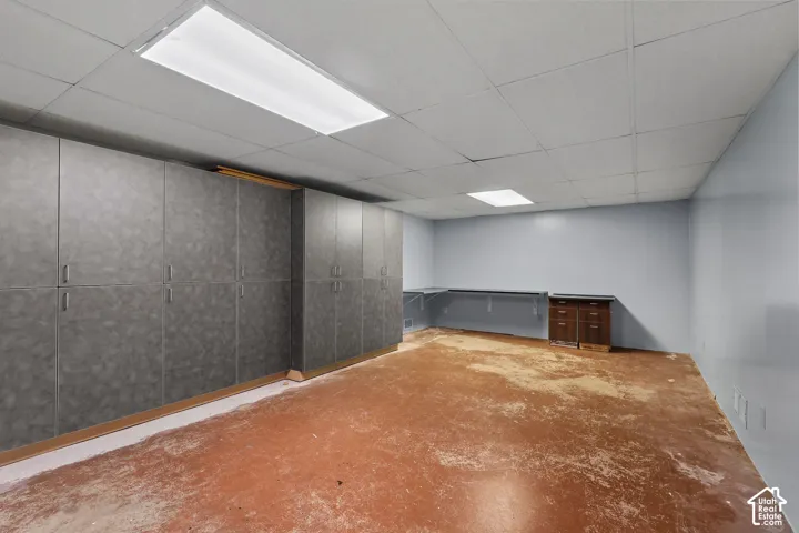 Expansive room featuring floor-to-ceiling built-in cabinetry, drop-ceiling panels with recessed lighting, and a solid-surface wall-mounted workspace