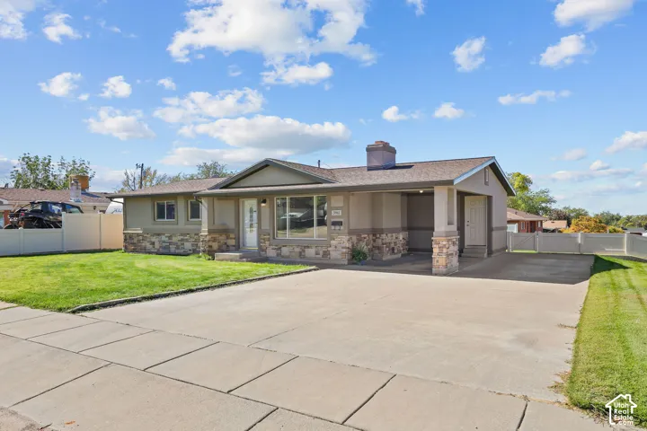 Single-story residence featuring a partial stone veneer exterior, an attached carport, a concrete driveway, and a fenced front lawn