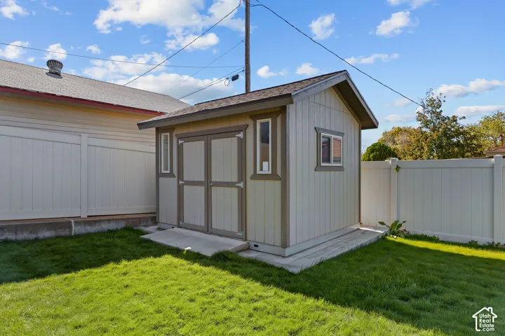 Detached storage structure featuring vertical siding, shingle roofing, double-door entry, integrated vertical windows, and a concrete foundation pad
