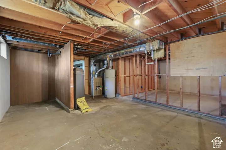 Unfinished basement space featuring exposed ceiling joists, concrete flooring, wood-paneled walls, and visible mechanical systems including a water heater and furnace