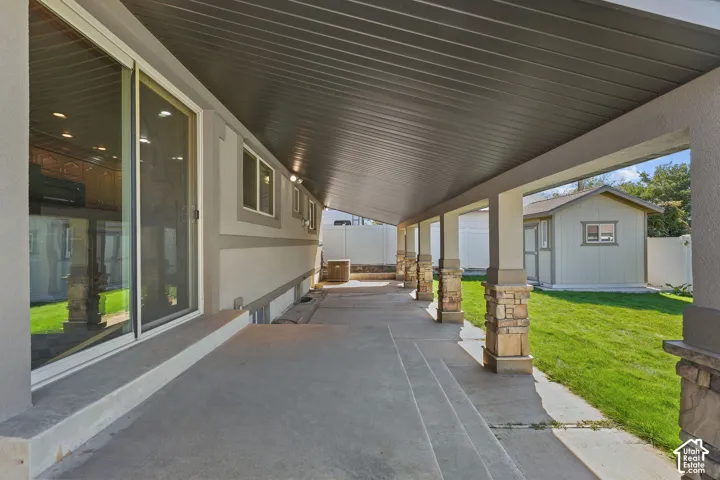 Covered concrete patio featuring stone-pillar supports and a paneled ceiling, providing access to the exterior via a sliding glass door