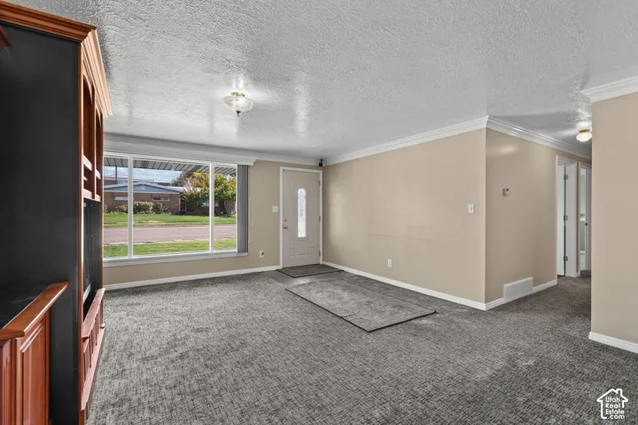 Living area featuring a large picture window, built-in wooden cabinetry, neutral wall paint, crown molding, and carpeted flooring
