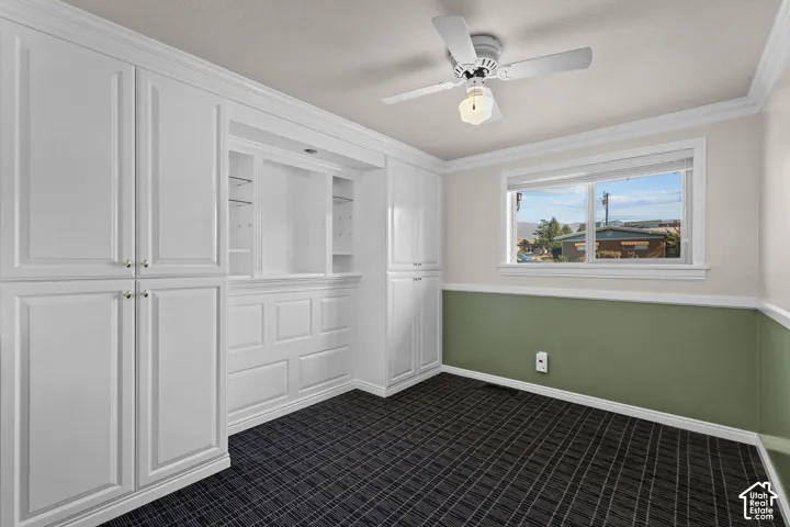 Built-in cabinetry with integrated shelving, crown molding, plaid patterned carpeting, a ceiling fan with light fixture, and horizontal sliding windows