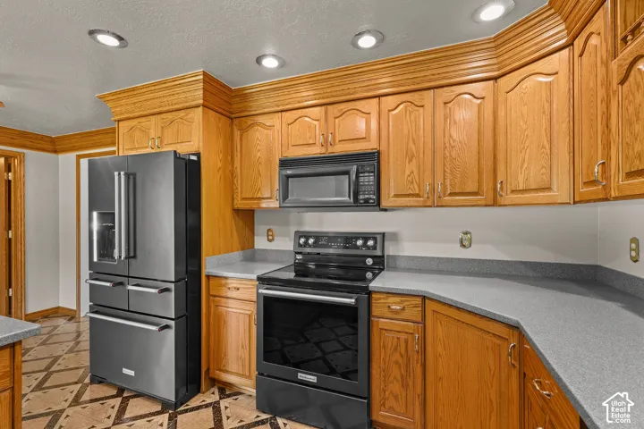 Kitchen featuring crown-molded oak cabinetry, grey solid-surface countertops, recessed lighting, and stainless steel appliances