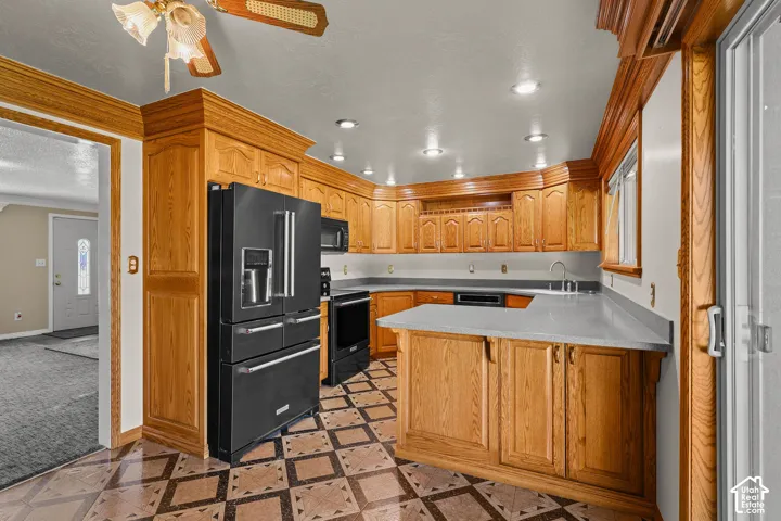 Kitchen featuring custom wood cabinetry with crown molding, solid-surface countertops, black integrated appliances, recessed lighting, and patterned tile flooring