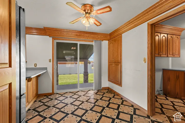 Kitchen area featuring geometric patterned tile flooring, wood cabinetry with crown molding, built-in floor-to-ceiling storage, a ceiling fan with integrated lighting, and a sliding glass door providing access to a covered patio