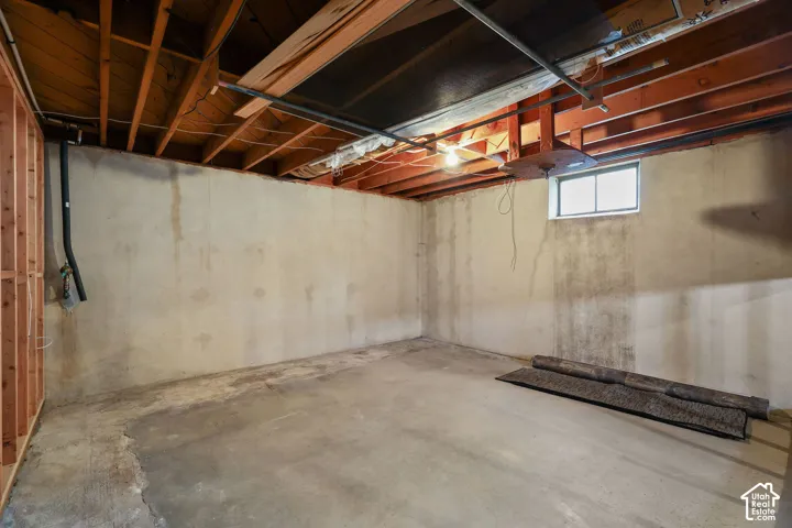 Unfinished interior space featuring exposed wood joist ceilings, concrete walls, concrete flooring, and a single-pane window