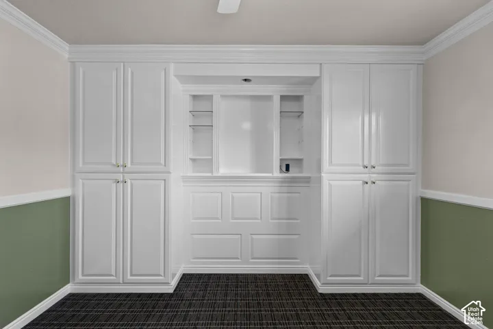 Built-in cabinetry featuring white shaker-style doors, glass shelving, recessed central alcove, and wainscot paneling details