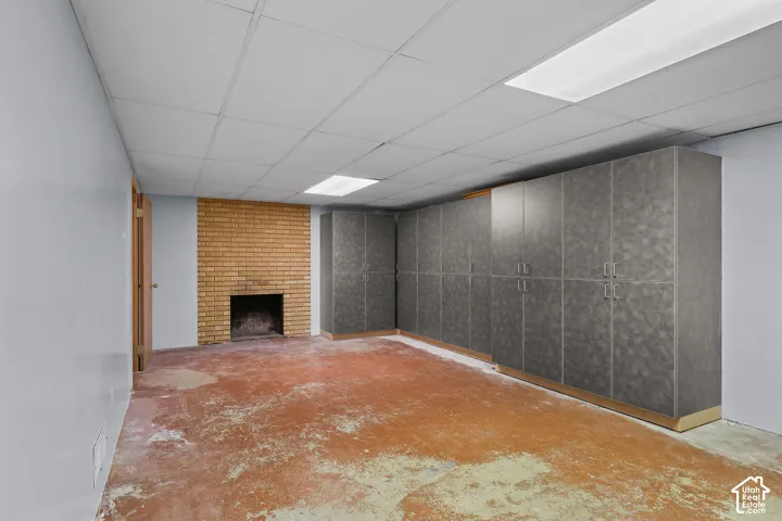 Interior space featuring a brick fireplace and expansive floor-to-ceiling built-in cabinetry with a textured finish, set under a dropped ceiling with recessed fluorescent lighting