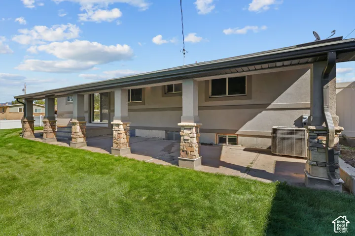 Covered concrete patio featuring stone-clad pillars, stucco siding, and a grass lawn