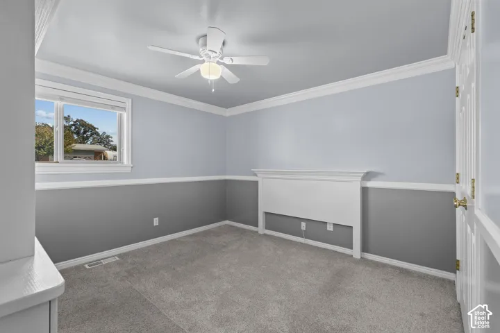 Room featuring dual-tone paint, crown molding, chair rail trim, built-in headboard, and a ceiling fan