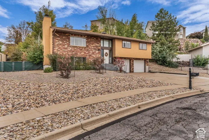 Split-level exterior featuring a brick and stucco facade, an attached two-car garage, and xeriscaped front grounds