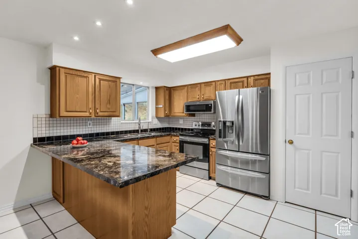 Kitchen featuring wood cabinetry, granite-finish countertops, stainless steel appliances, tiled backsplash, and ceramic floor tiling