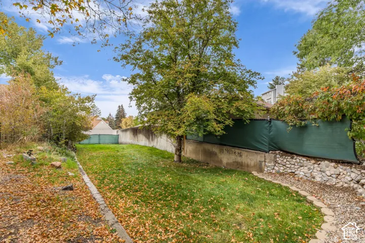 Backyard featuring a grass lawn, mature trees, stone retaining wall, and gravel border