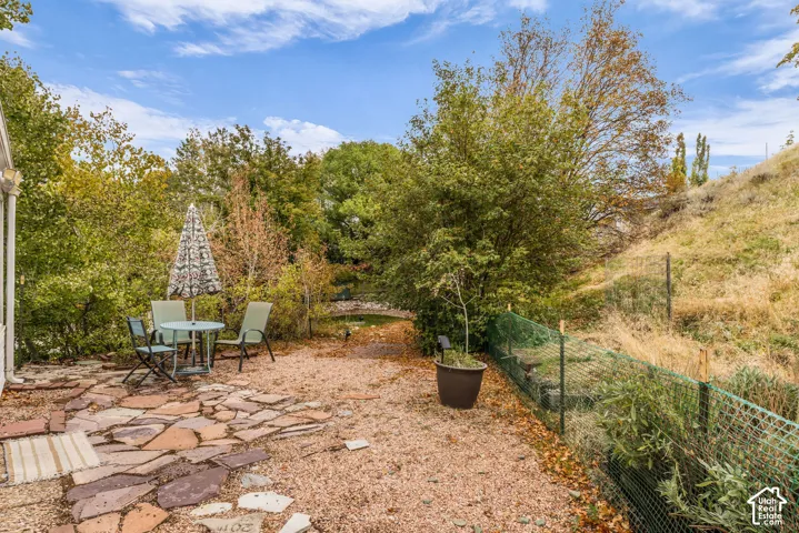 Backyard featuring a flagstone patio, gravel surfacing, mature trees, and tiered hillside terrain